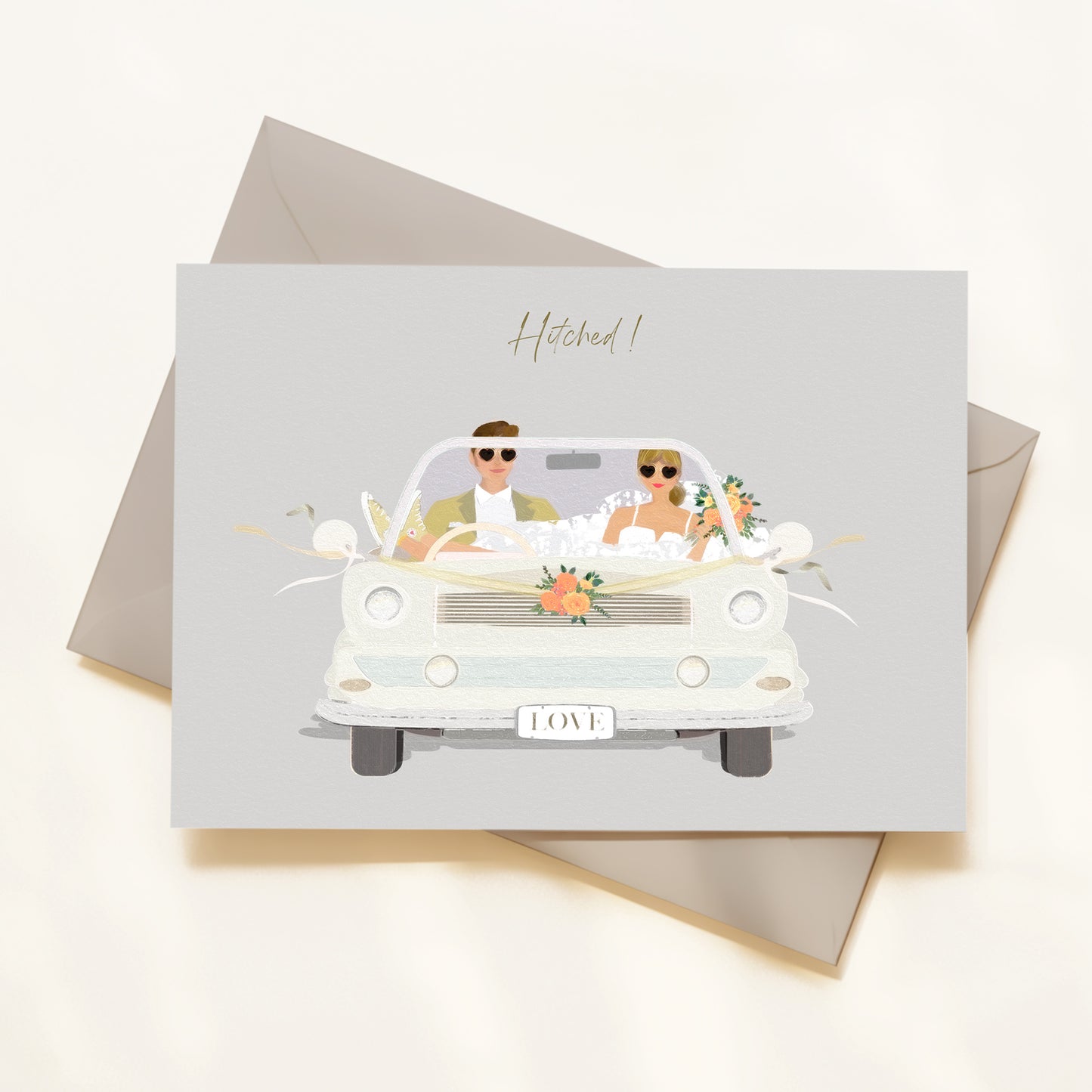 Greeting card with illustration of a couple in a car, text 'Hitched!', on a light gray background.