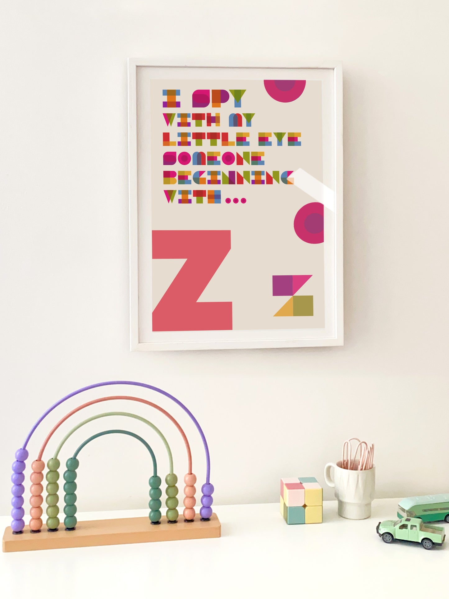 "Z" Framed children's art with colourful letters on a white wall, accompanied by educational toys.