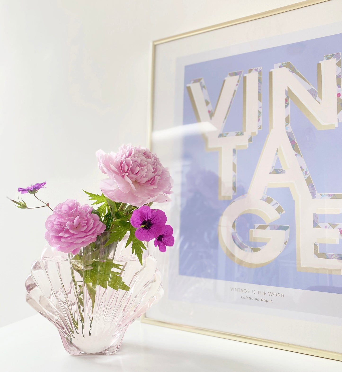 Shell-shaped vase with pink flowers next to a framed artwork with 'VINTAGE' text on a white background