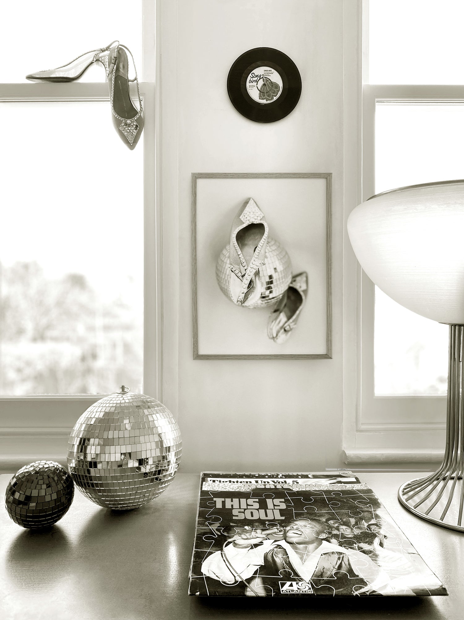 A framed shoe print surrounded by decorative items including a disco ball, record, and vinyl album covers on a surface with a window in the background.