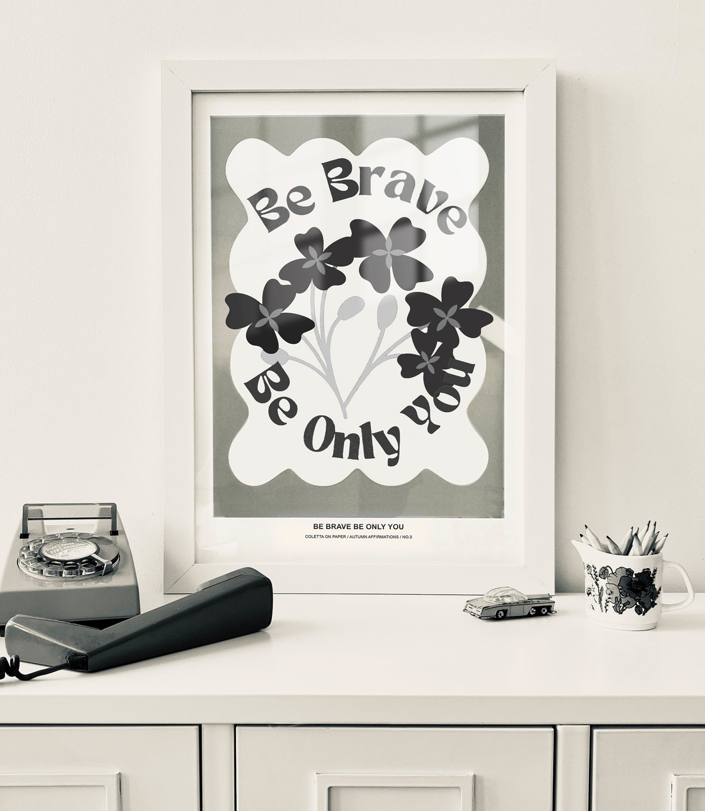 Framed poster with motivational quote 'Be Brave Be Only You' on a locker style cabinet with decorative items.