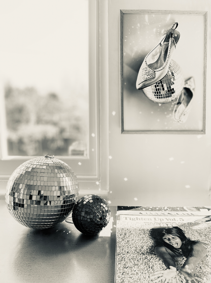 Decorative mirror balls and framed picture of high heels with disco ball on a wall.