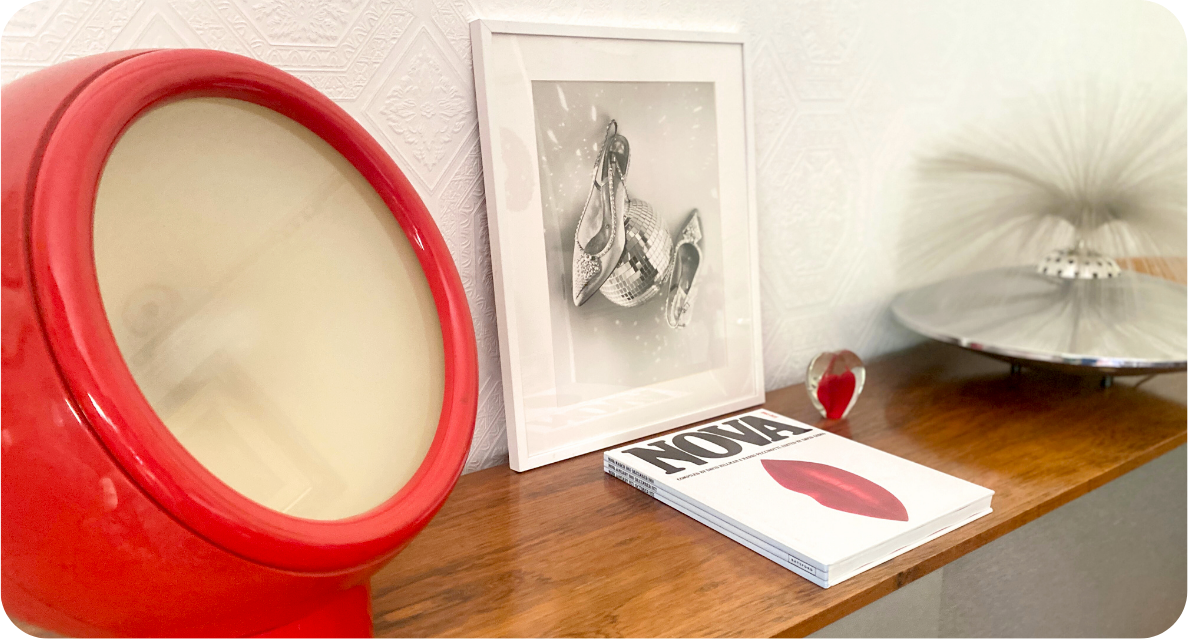 Sideboard with mid century modern table lighting and framed print of a disco ball and shoes with decorative heart paperweight and coffee table book on surface.