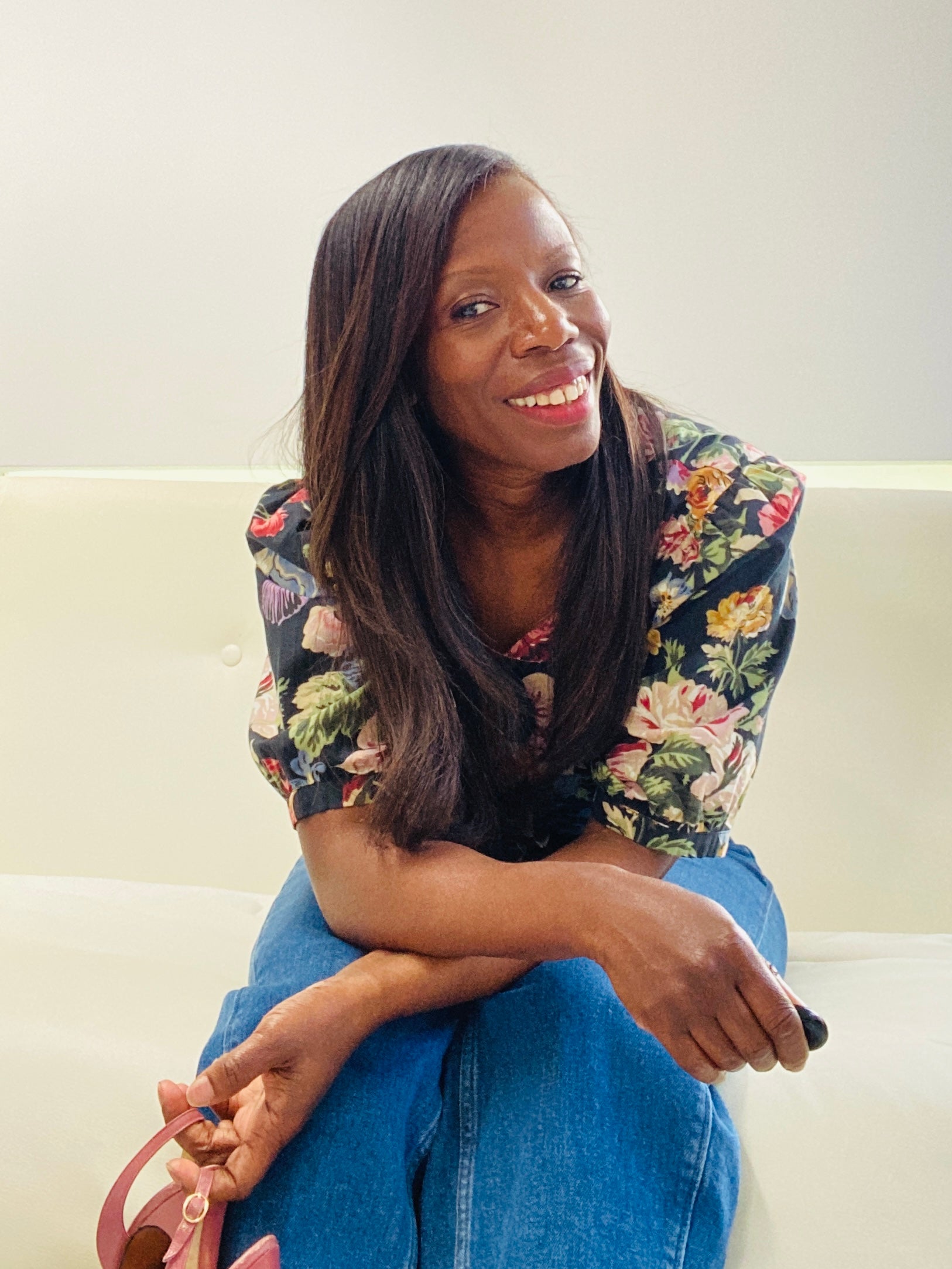 Colette sitting on a couch wearing a vintage floral top and blue jeans, holding a pink vintage shoes.