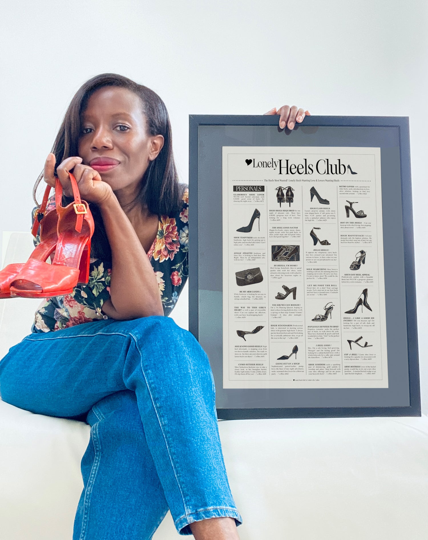 Colette holding a framed poster with shoe illustrations and a red shoe.