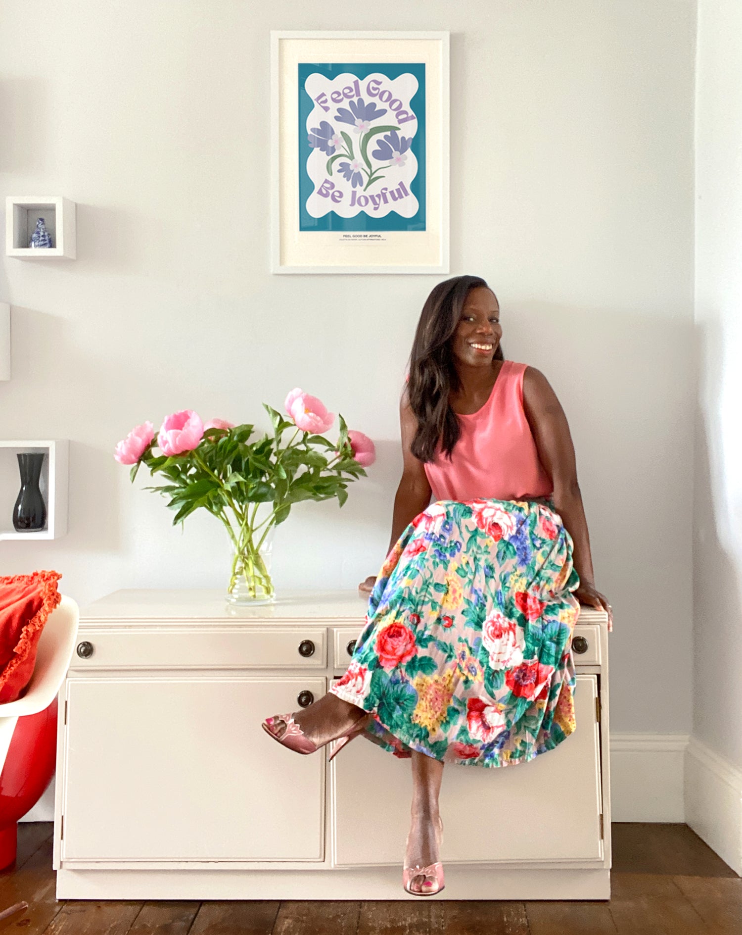 Woman sitting on a white cabinet with flowers and a colorful poster in the background