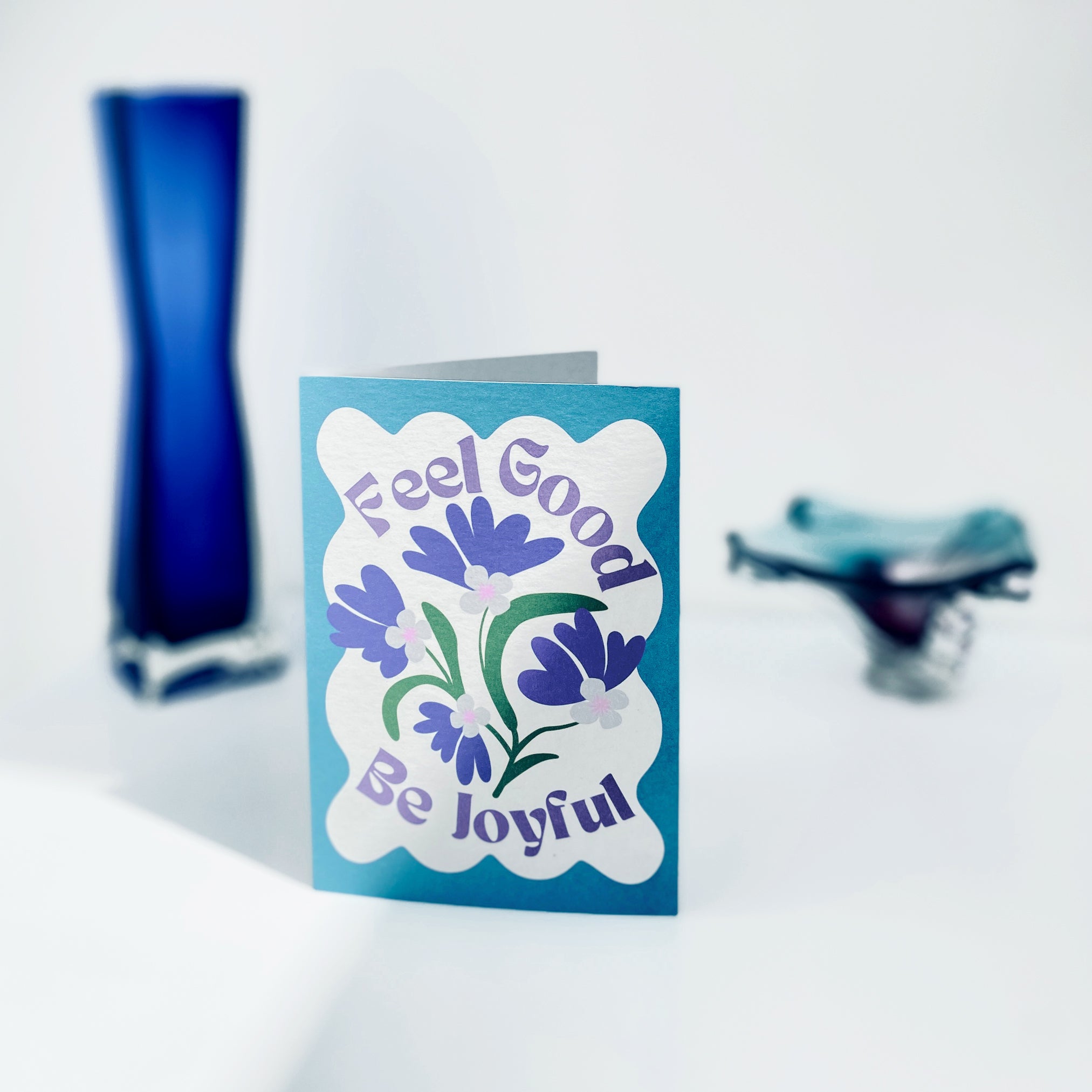 Blue card with floral design and text 'Feel Good Be Joyful' on a white background