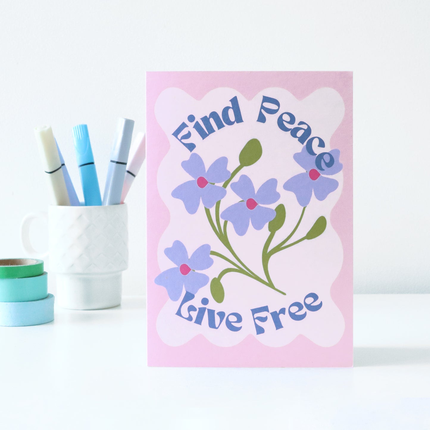 Card with floral design and text 'Find Peace, Live Free' on a pink background, with markers and tape in the background.