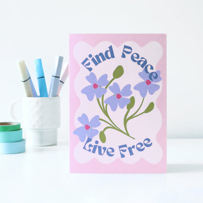 Card with floral design and text 'Find Peace, Live Free' on a pink background, with markers and tape in the background.