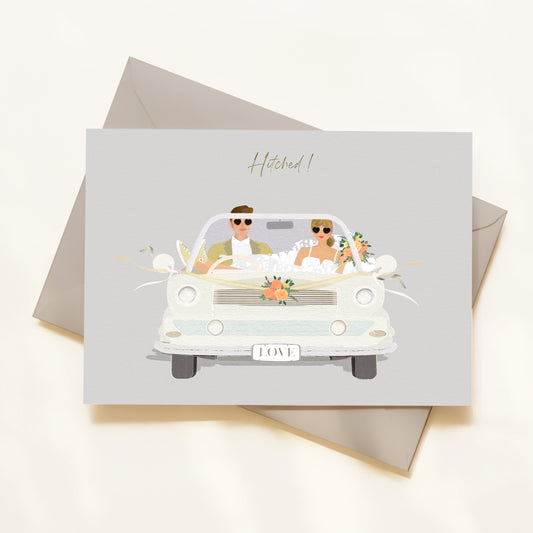 Greeting card with illustration of a couple in a car, text 'Hitched!', on a light gray background.