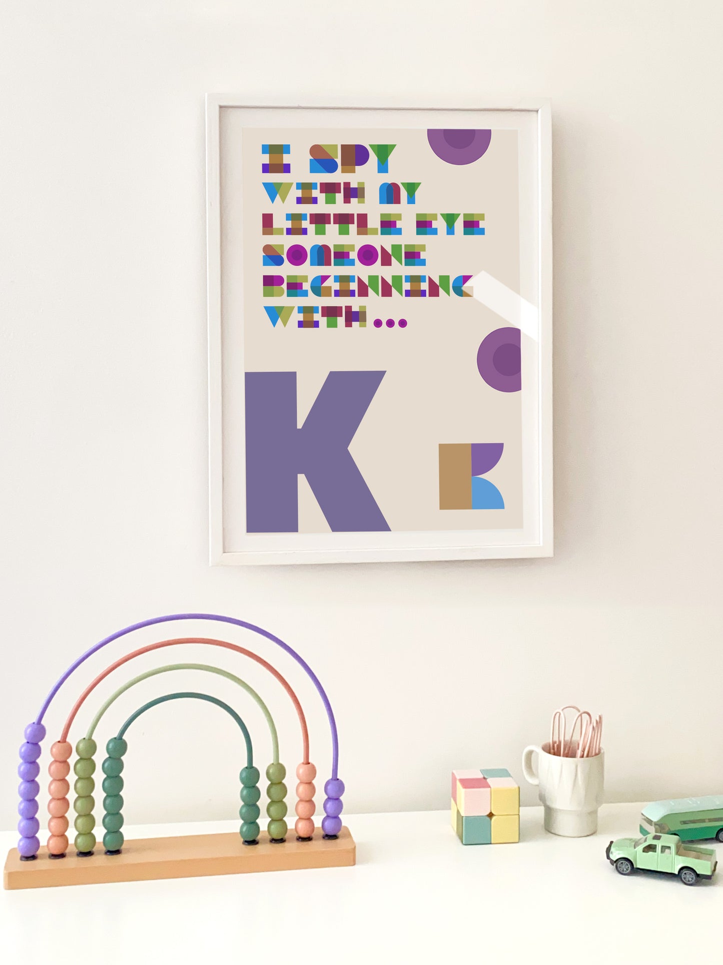 Framed children's art with colorful letters on a white wall, accompanied by educational toys.