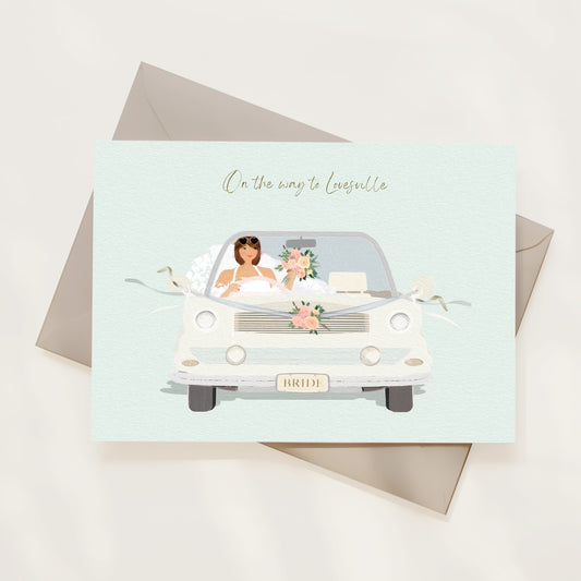 Card with illustration of a bride in a car, 'On the way to Lovesville' text, and envelope on a light background