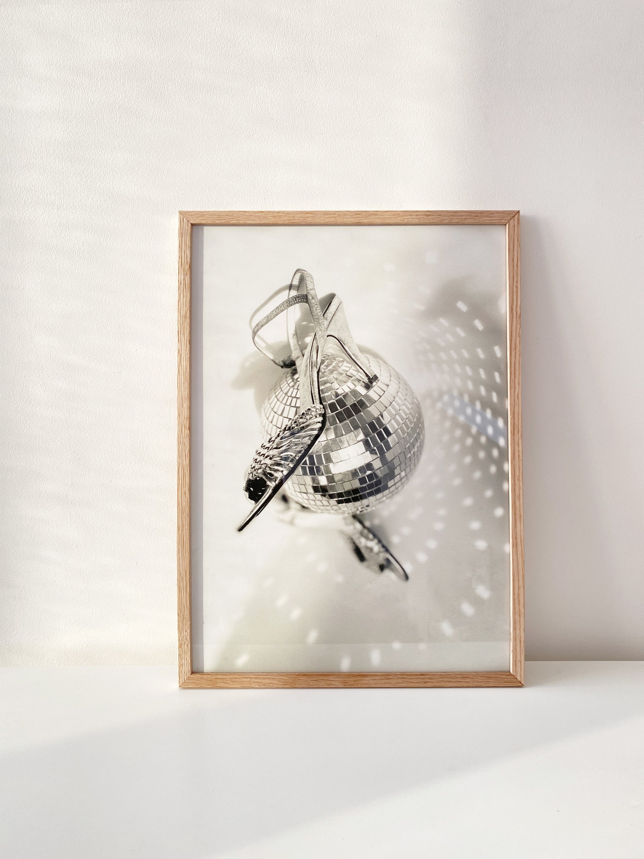 Framed artwork of a disco ball and vintage silver heels on a white wall