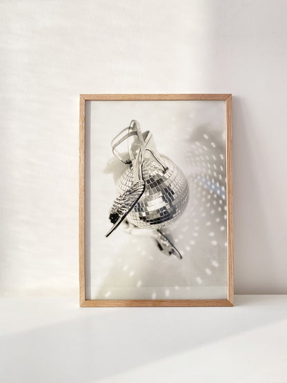 Framed artwork of a disco ball and vintage shoes on a white wall
