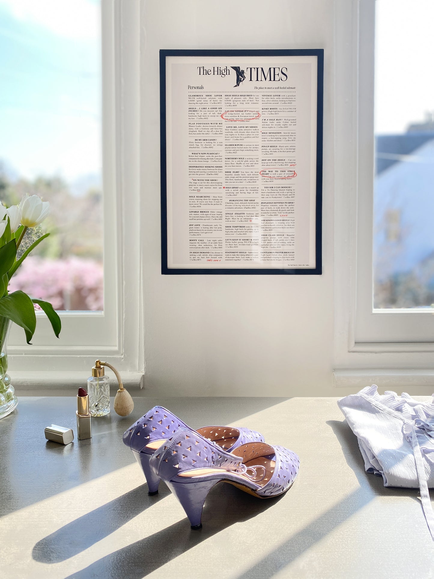A framed 'The High Times' magazine style art print displayed on a window sill with a pair of purple high heels shoes in front of it.