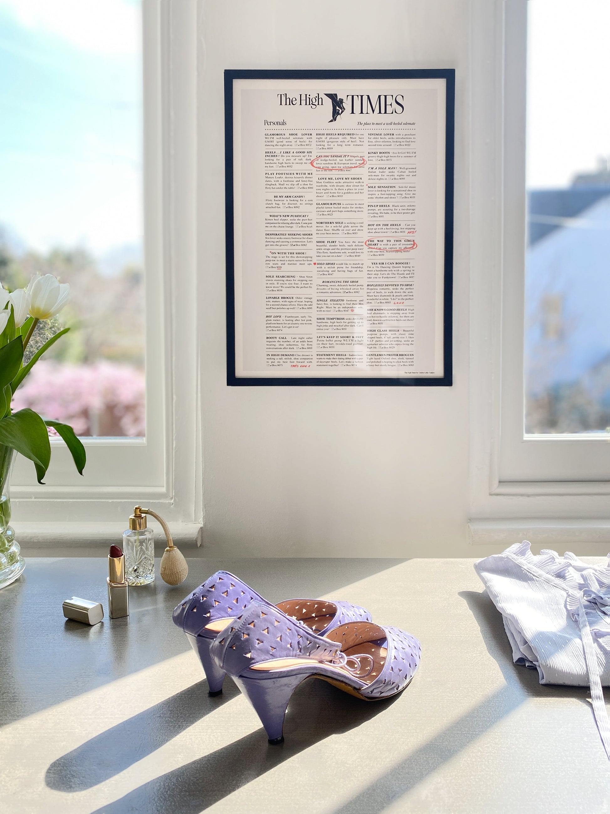 A framed 'The High Times' magazine style art print displayed on a window sill with a pair of purple high heels shoes in front of it.