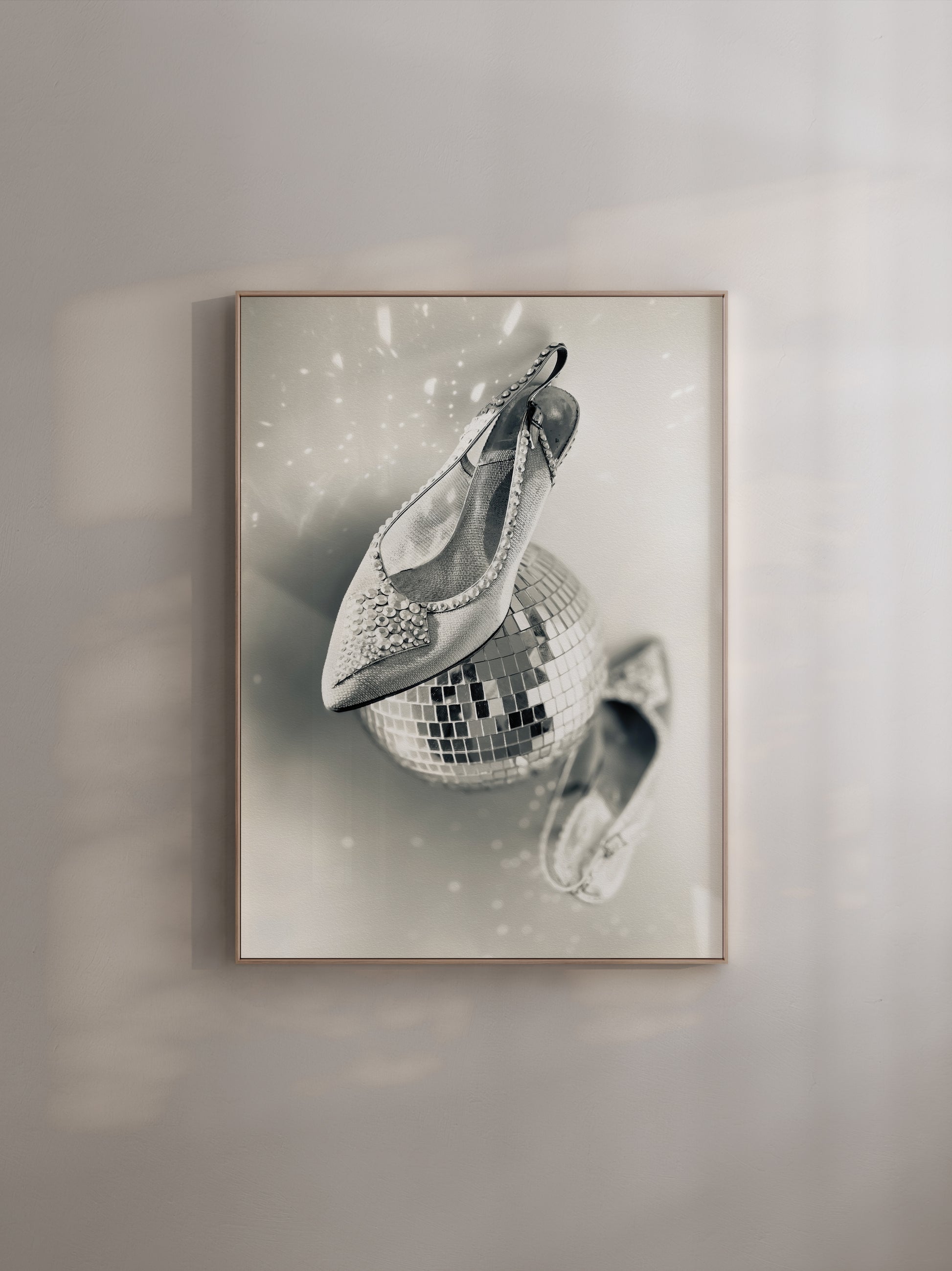 Framed artwork of a disco ball with shoe son a light grey wall.