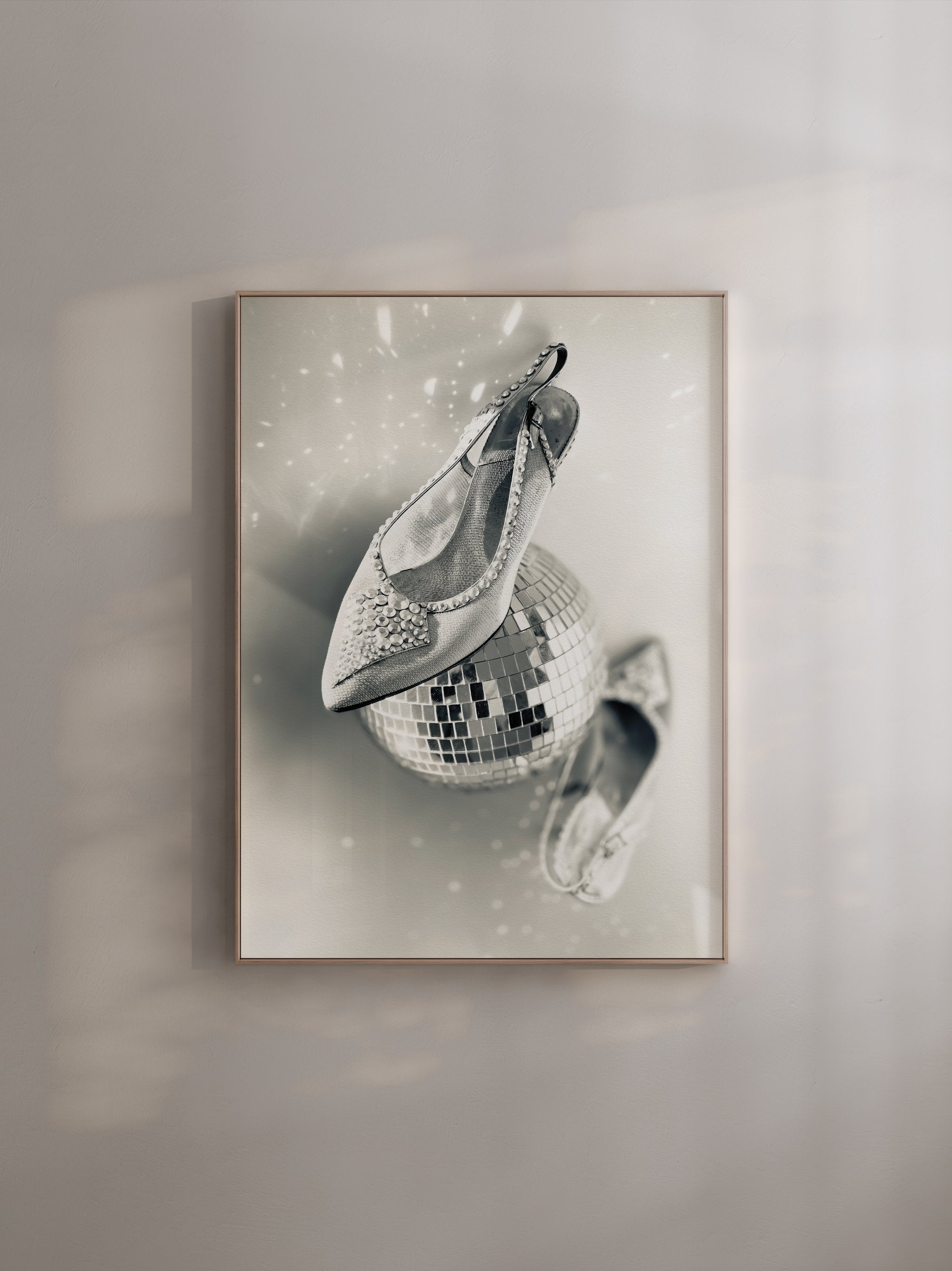Framed artwork of a disco ball with shoe son a light grey wall.