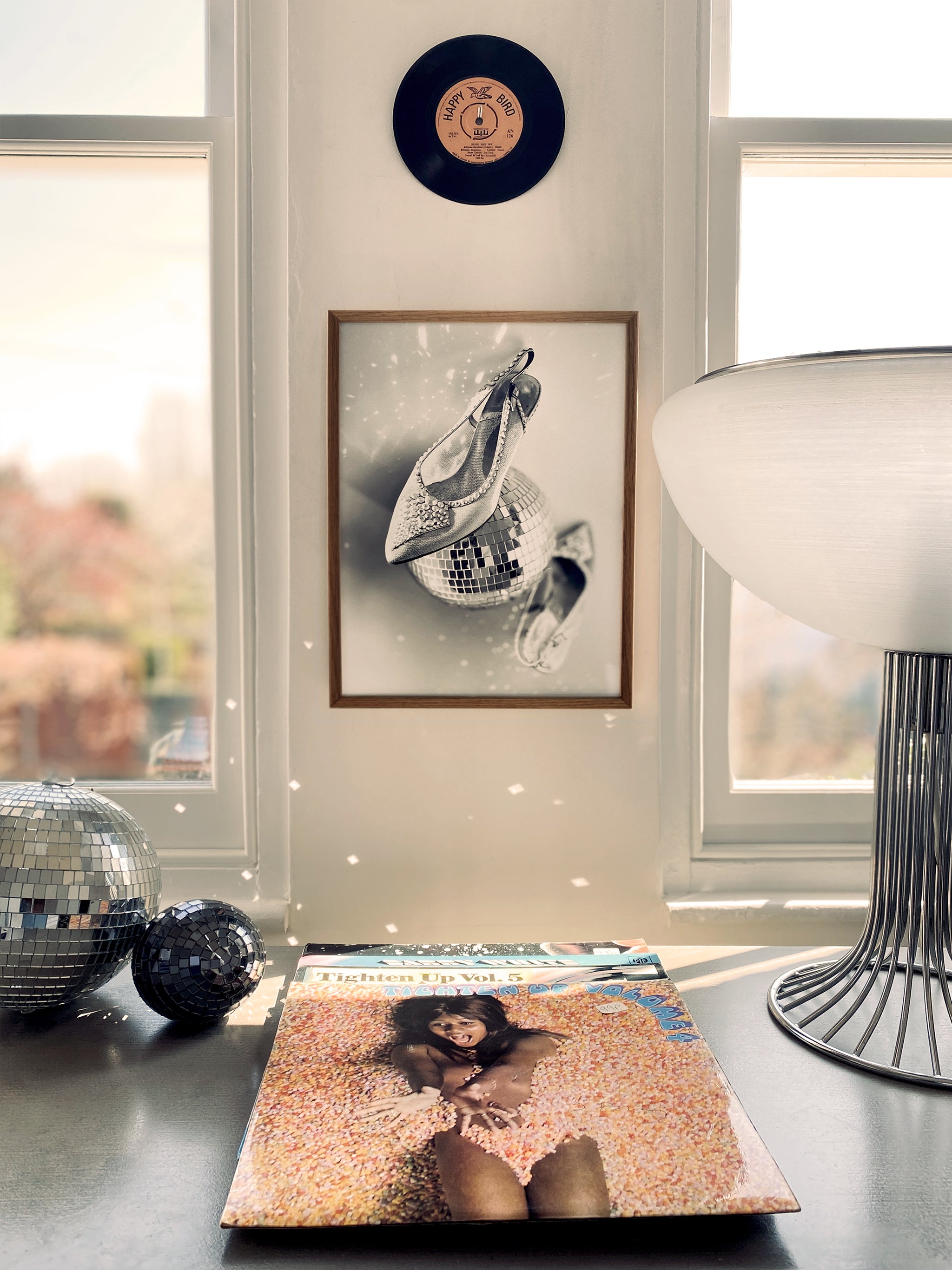 Decorative items on a table with a framed picture of a shoe, a lamp, and vinyl records.
