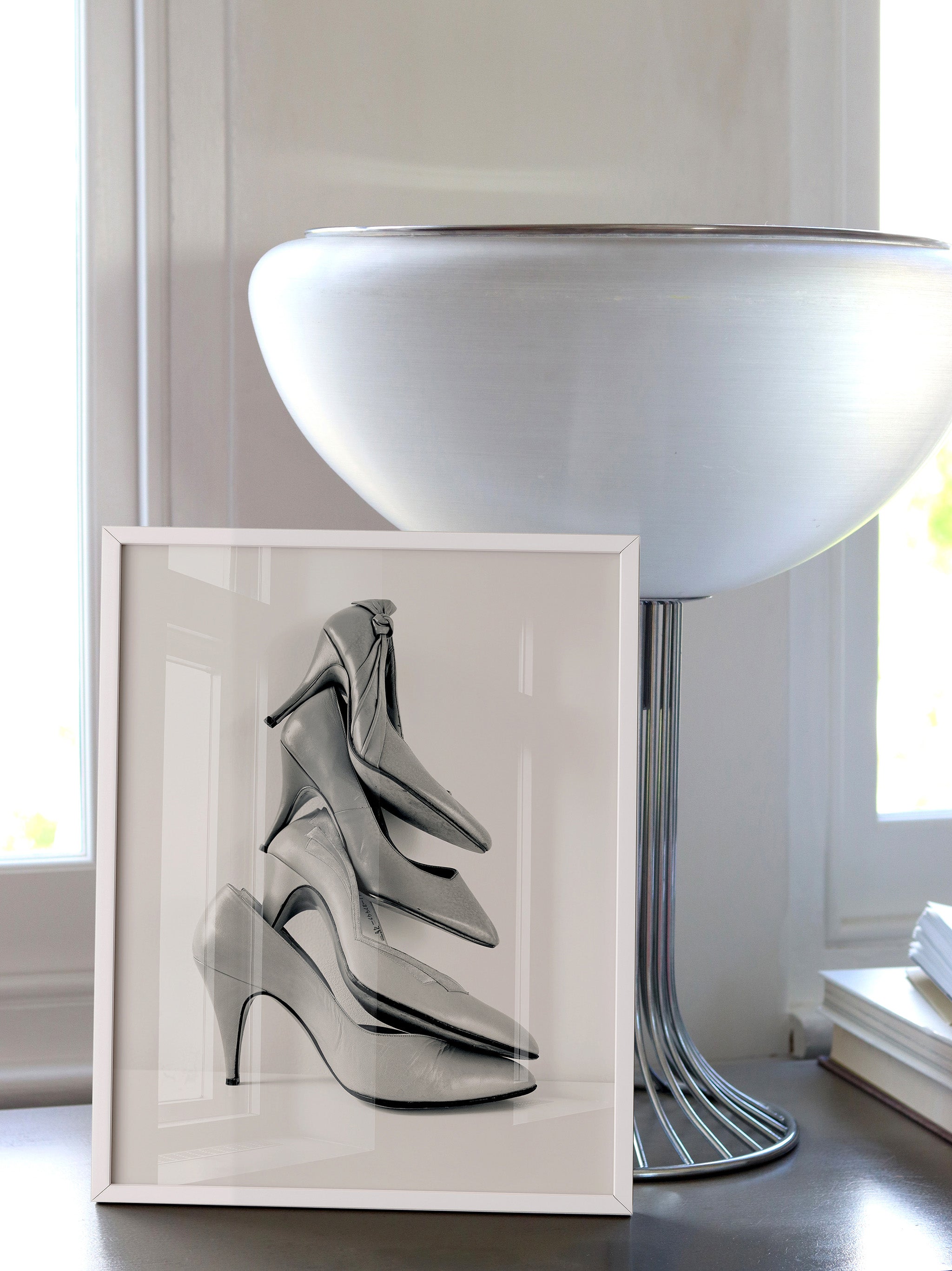 Framed artwork of high-heeled shoes on a table next to a mid-century modern vintage light.