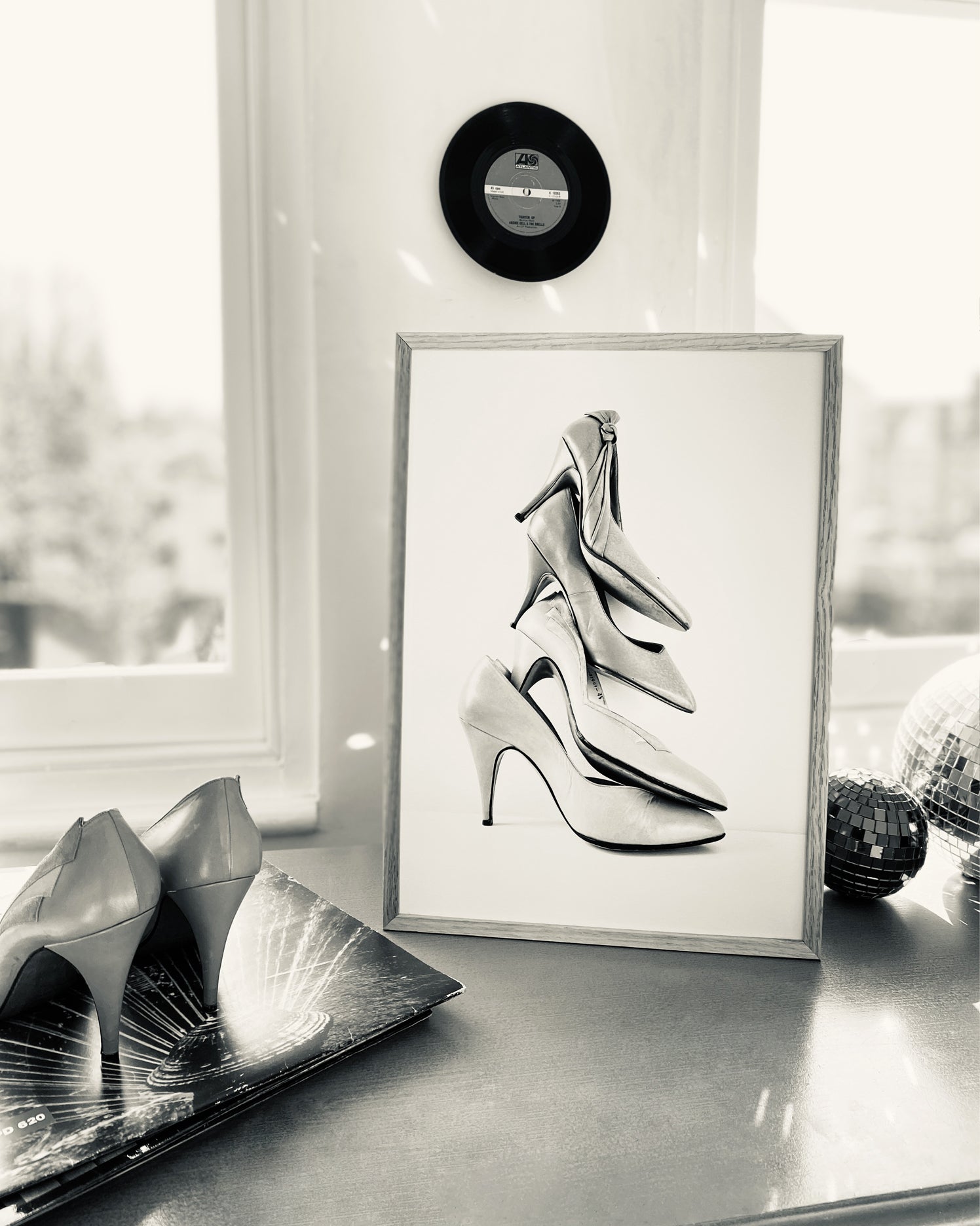 Framed black and white art print of high heels on a table with a window in the background