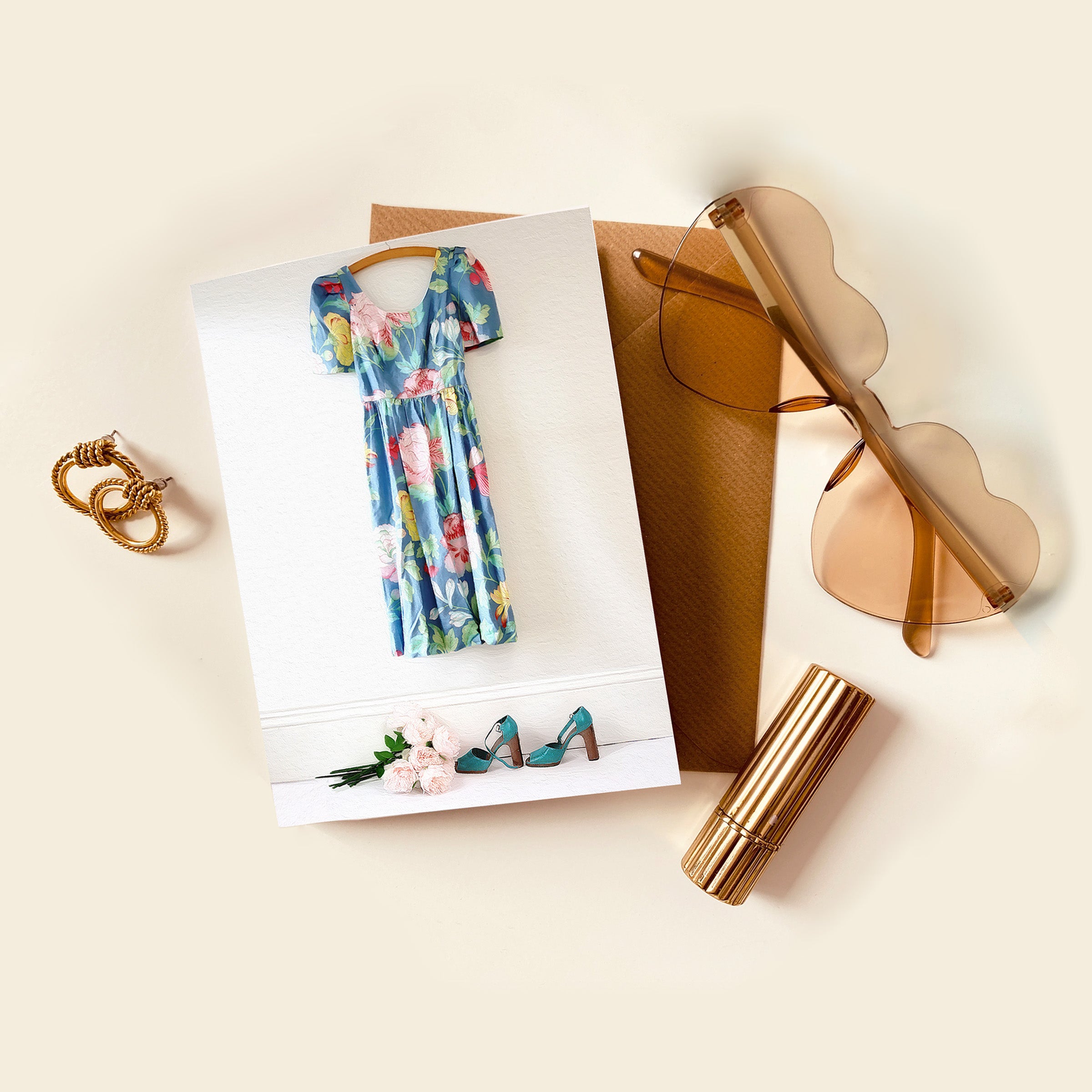 Floral dress on a card with sunglasses, purse, and lip gloss on a light background