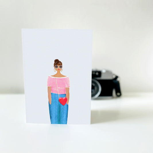 Card with illustration of a person wearing sunglasses and holding a heart shaped bag, with a blurred camera in the background.